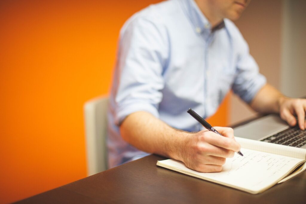 Man is working with a computer and making notes.