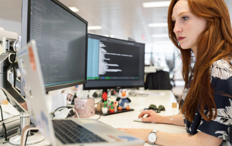 A woman works at a computer and writes program code.