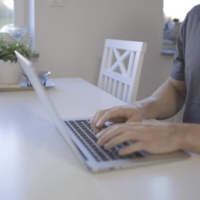 A person working on a laptop with a bright, sunlit room in the background