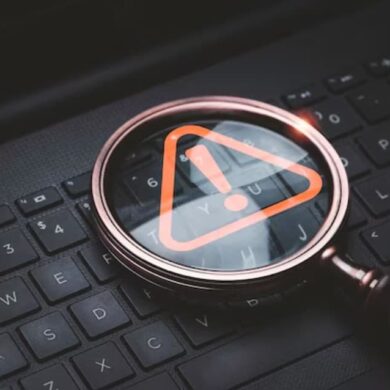 a magnifying glass with an orange caution warning sign on the keyboard of a laptop