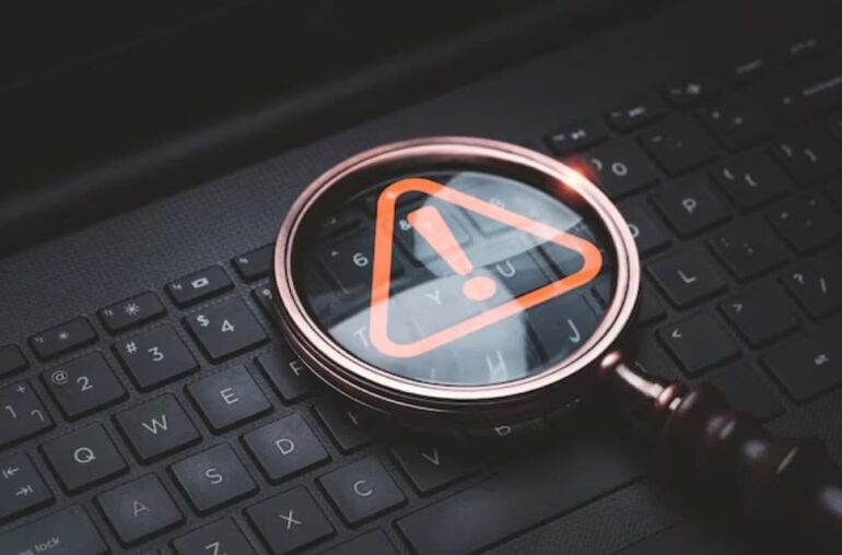 a magnifying glass with an orange caution warning sign on the keyboard of a laptop