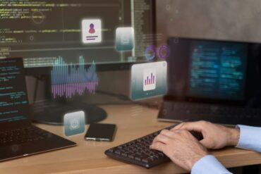 Hands typing with digital data icons over a dual-screen coding setup