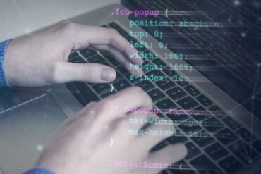 Hands writing program code on a laptop